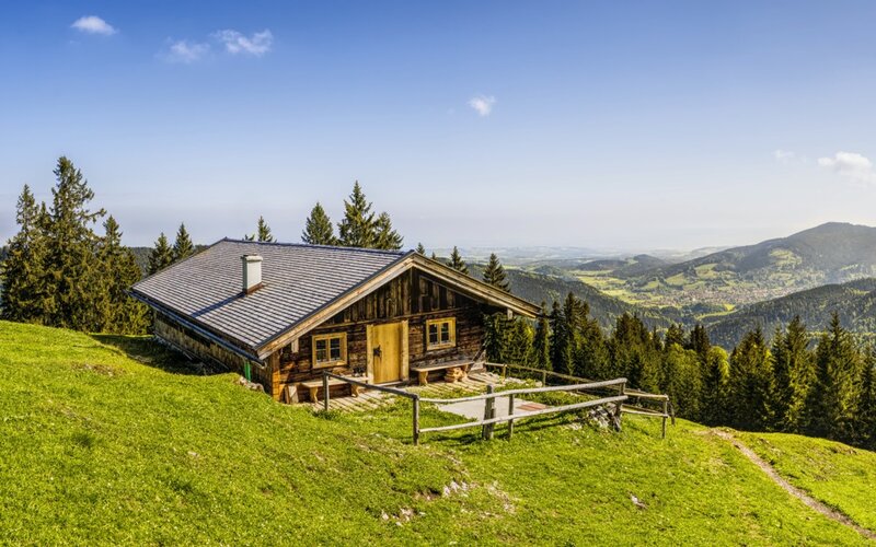 Berghütte auf einer grünen Alm vor bewaldeten Bergen in Bayern