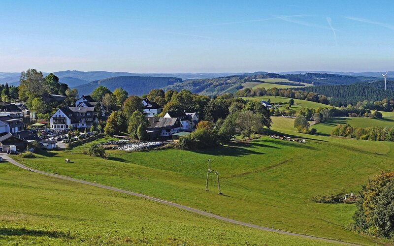 Dorf zwischen grünen Wiesen und bewaldeten Hügeln im Sauerland
